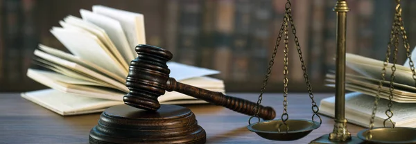 Hukuk ve Adalet sembolleri ahşap masa üzerinde bulanık kitap arkaplanı.