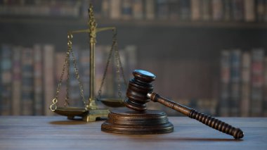 Hukuk ve Adalet sembolleri ahşap masa üzerinde bulanık kitap arkaplanı.