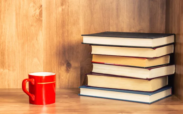 Cup of coffee with pile of closed books on wooden background
