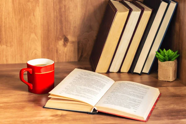 Pile of closed books and open book with cup of coffee on wooden background.