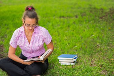 Bir fincan kahveyle çimenlerin üzerinde kitap okuyan bir kadın..
