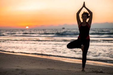 Gün batımında plajda yoga yapan bir kadın.