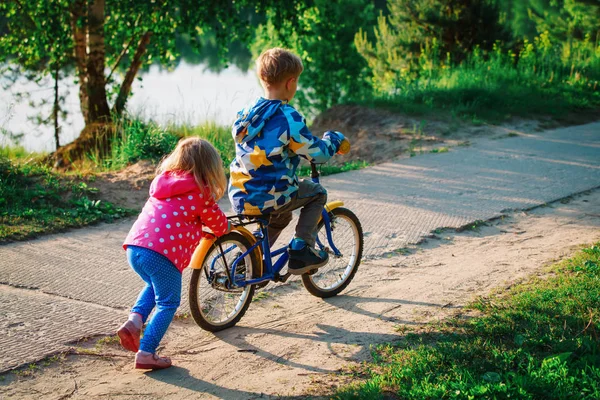 Kleines Mädchen schubst kleinen Jungen auf Fahrrad in der Natur — Stockfoto