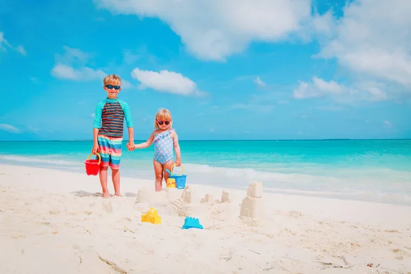 Niño y niña juegan con arena en la playa —  Fotos de Stock