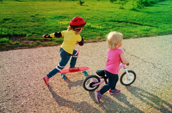 Niedliche glückliche Mädchen auf Fahrrad und Skateboard fahren — Stockfoto