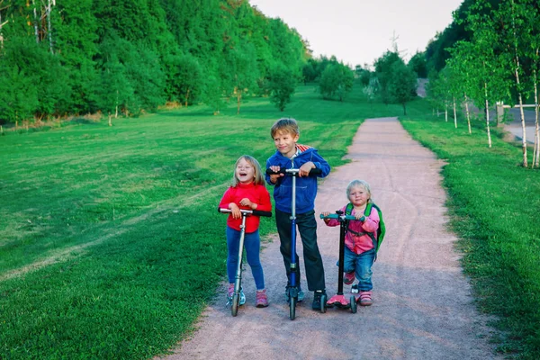 Bambini felici bambino e ragazze che cavalcano scooter in natura — Foto Stock