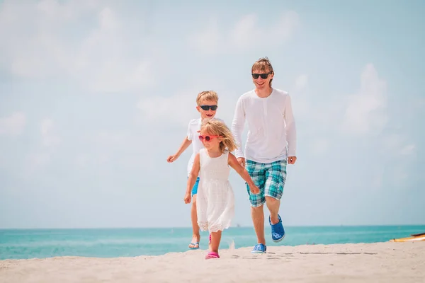 Far med liten sønn og datter som leker, løper på stranda – stockfoto
