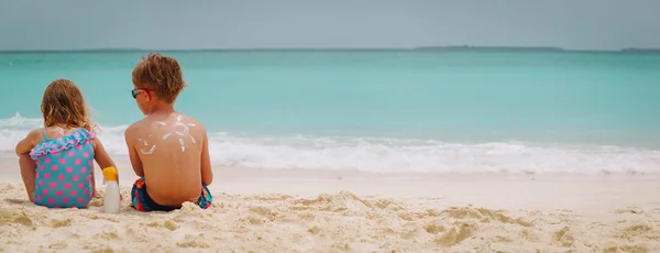 VN-bescherming - kleine jongen en meisje met zonnebrandcrème op strand — Stockfoto