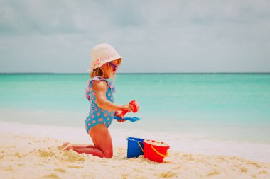 Tatlı küçük kız kumsalda kumla oynuyor.