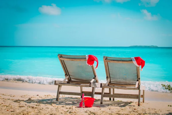 Natal em salões de cadeira de praia com chapéus de Santa no mar — Fotografia de Stock