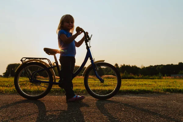 Bambina in sella alla bici al tramonto, sport per bambini — Foto Stock