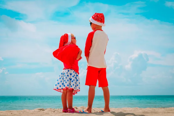 Menino e menina com presentes comemorando o Natal na praia tropical — Fotografia de Stock