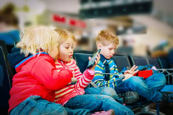 Niños - mirando el panel táctil y el teléfono móvil en el aeropuerto —  Fotos de Stock
