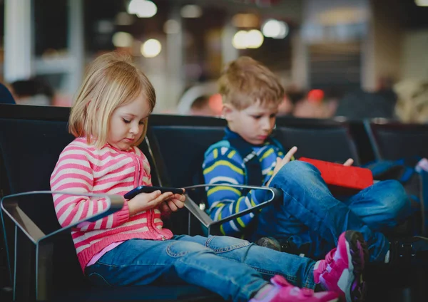 Niño y niña mirando almohadilla táctil y teléfono móvil en el aeropuerto —  Fotos de Stock