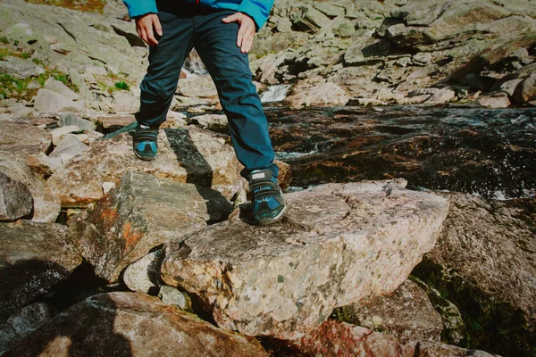 little boy hiking in mountains crossing waterfall, focus on boots