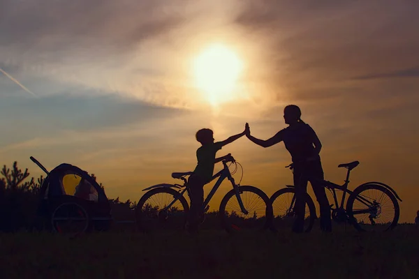 Feliz família mãe com crianças andar de bicicleta ao pôr do sol — Fotografia de Stock