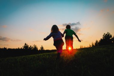 Silhouette mutlu çocuk ve oyun günbatımında çalışan kız