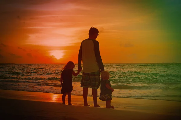 Padre y dos niños caminando en la playa al atardecer — Foto de Stock