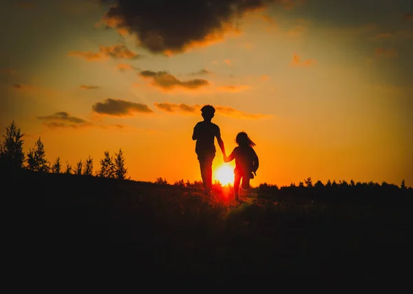 Silhouette de joyeux garçon et fille courir jouer au coucher du soleil — Photo