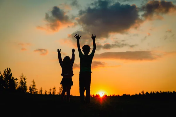 Silhouettes heureux garçon et fille profiter du coucher du soleil nature — Photo