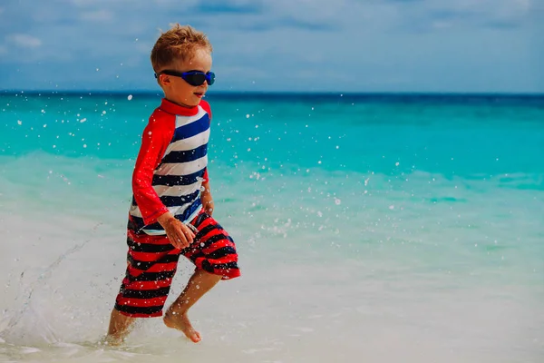 Jongetje lopen spetterend water op strand — Stockfoto