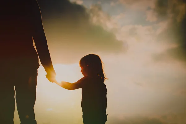 Silhouette della bambina che tiene la mano del genitore al tramonto — Foto Stock