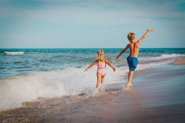 Klein meisje en jongen vliegen lopen spelen met golven op het strand — Stockfoto