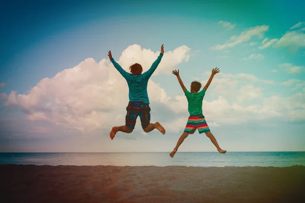 Far och son har roliga hoppa på sunset beach — Stockfoto