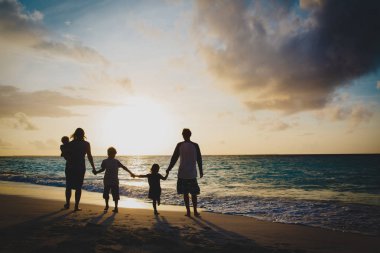 Ağaç çocukları olan mutlu aile gün batımında tropikal sahilde yürür.