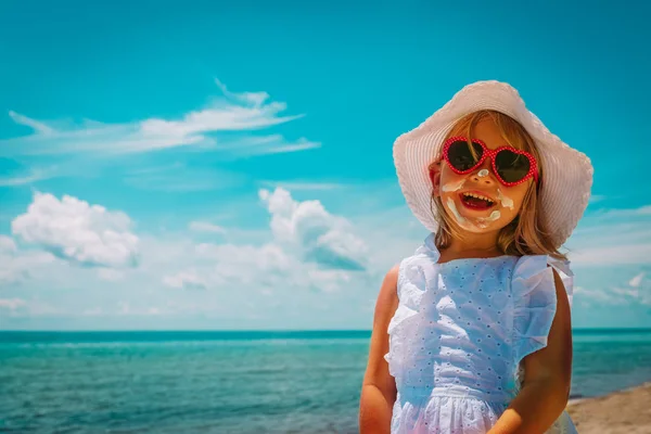 Защита от солнца - счастливая маленькая девочка с кремом для загара на пляже — стоковое фото