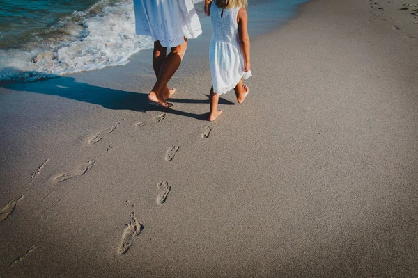 Mãe e filha andando na praia deixando pegada na areia — Fotografia de Stock