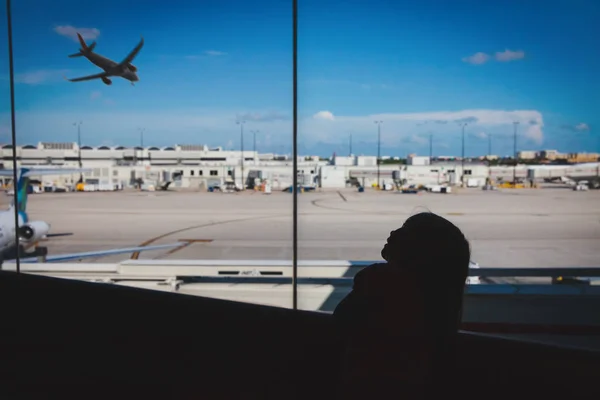 Маленька дівчинка чекає в аеропорту, дивлячись на літаки, сімейні подорожі — стокове фото