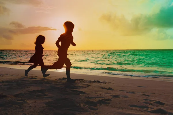 Kleine Jungen und Mädchen laufen am tropischen Strand bei Sonnenuntergang spielen — Stockfoto
