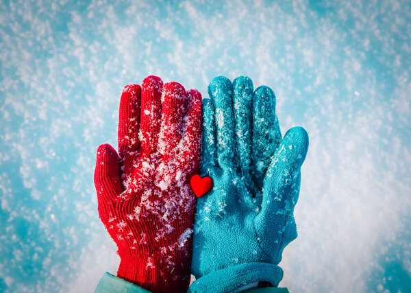 Hands in gloves holding heart in winter nature