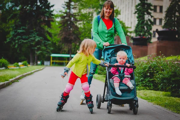 Активная семья - мать и маленькая девочка на роликовых коньках с коляской в городе — стоковое фото