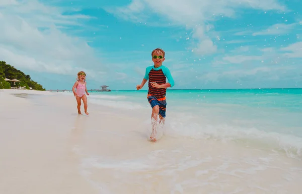 Klein meisje en jongen lopen spelen met golven op het strand — Stockfoto