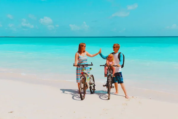 Šťastná rodina s malou holčičku na kolech na pláži — Stock fotografie