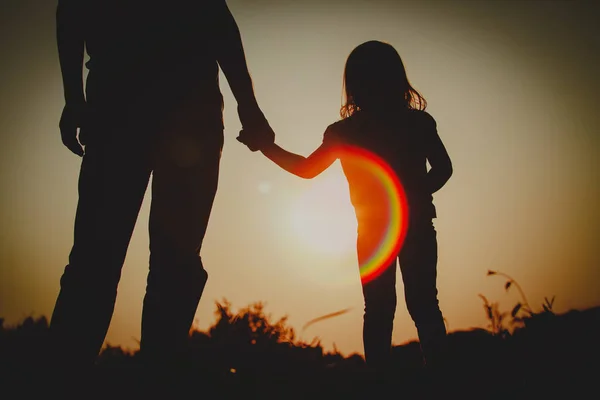 Silhuett av liten flicka som håller föräldrarnas hand vid solnedgången — Stockfoto