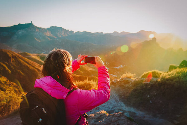Young tourist making mobile phone photo of sunset in mountains, travel concept