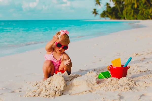 Милая маленькая девочка играет с песком на тропическом пляже — стоковое фото