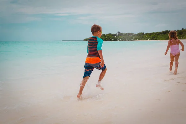 Bambina e ragazzo corrono, i bambini giocano con le onde sulla spiaggia — Foto Stock