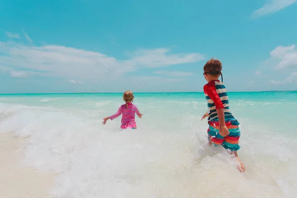 Malou holčičku a chlapce spustit hrát s vlnami na pláži — Stock fotografie