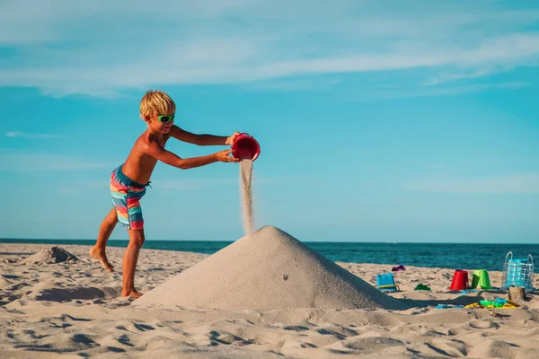 cute boy play with sand at sea, kid building castle on tropical beach