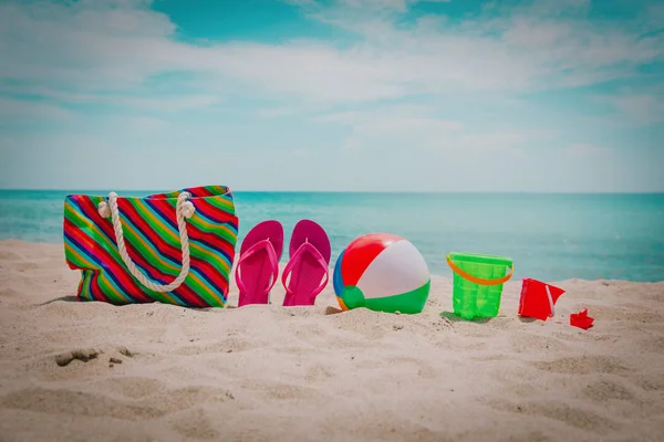 Torba, klapki japonki i dzieci zabawki na tropikalnej plaży — Zdjęcie stockowe