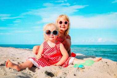 Şirin küçük kızlar kumsalda kumla oynuyorlar.