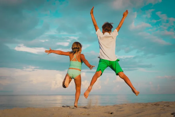 Mutlu küçük erkek ve kız plajda oyna, çocuklar sevinç atlamak — Stok fotoğraf