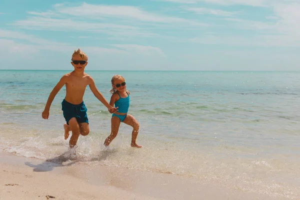 Дети: девочка и мальчик играют с волнами на пляже — стоковое фото