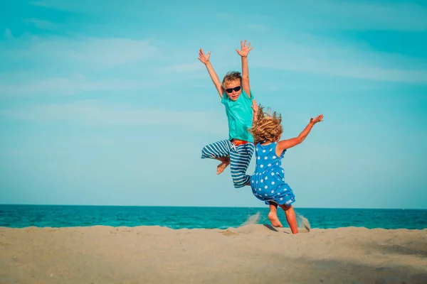 En glad liten gutt og jente leker og hopper på stranda – stockfoto