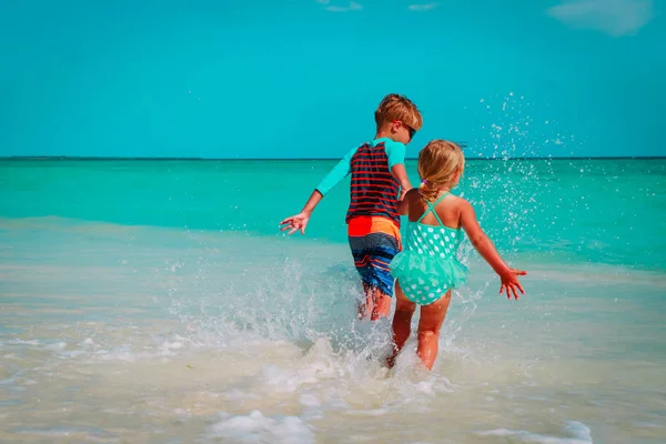 Malou holčičku a chlapce spustit hrát s vodou na pláži — Stock fotografie