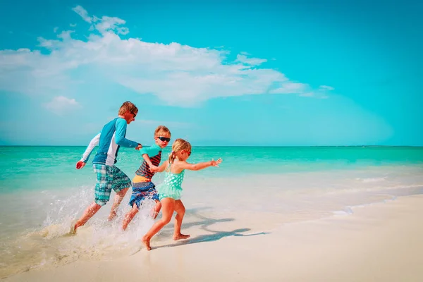 Vader met kinderen spelen met water lopen op strand — Stockfoto